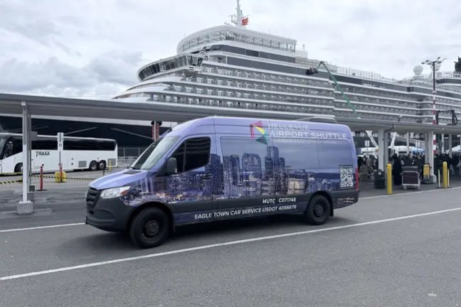 Shuttle van parked near cruise ship terminal on a cloudy day.
